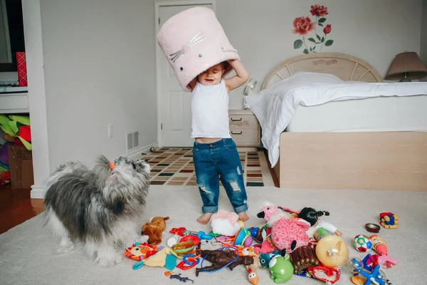 可爱可爱有趣的蹒跚学步的小女孩 头上带着玩具盒 小孩子在家里玩玩具 真正的家庭生活方式 带着宠物狗的小孩有趣而难忘的童年时光 — 图库照片