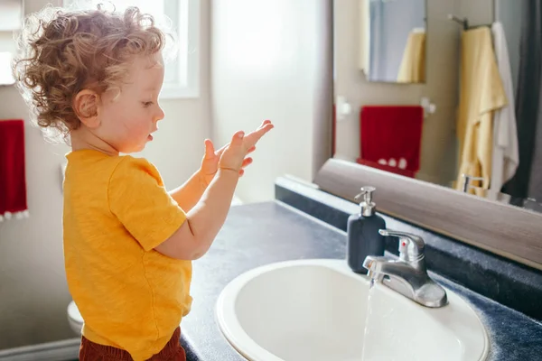 小さな白人の少年は自宅のバスルームで手を洗う 子供のための健康衛生と朝のルーチン 水で遊ぶかわいい面白い子供 子供は体の探索を学ぶ ストック画像