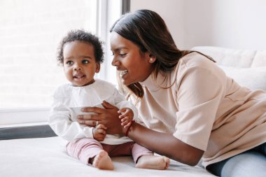 Mutlu gülümseyen genç Hintli anne siyah bebek kızıyla oynuyor. Aile melezi insanlar, anne ve çocuk evde sarılıyorlar. Çocuk bebekle samimi bir yaşam tarzı.. 