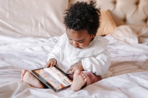 Mixed race African black toddler baby girl watching cartoons on tablet. Ethnic diversity. Little kid child using technology. Early age education development. Video chat, video call.