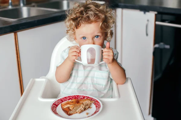 可爱的高加索卷曲男孩坐在高高的椅子上 吃着自制的苹果派 喝着杯子里的果汁 儿童的健康饮食 幼儿独立进食 — 图库照片
