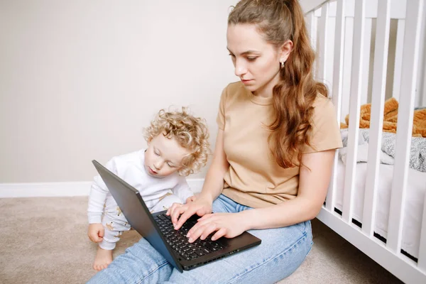 家庭からラップトップで働いている赤ちゃんを持つ白人の母親 子供の幼児とのフリーランスのビジネス女性の職場 ビデオチャットコール 家にいるシングルマザー稼ぐお金で遠い仕事でオンライン — ストック写真