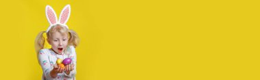 Şirin sevimli sürpriz pembe Paskalya tavşanı kulaklı, sarı arka planda yumurta tutan Kafkas kızı heyecanlandırdı. Komik çocuk geleneksel Hıristiyan bayramını kutluyor. Web başlığı.