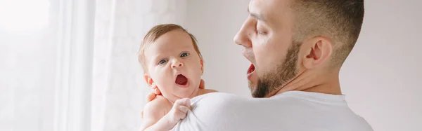 Fathers Day holiday. Caucasian father holds yawning newborn baby. Authentic lifestyle candid funny moment. Single young dad family life concept. Web banner header.