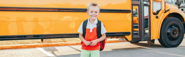 Happy smiling Caucasian boy student with backpack near yellow bus on first September day. Education and back to school in autumn fall. Child kid on schoolyard outdoors. Web banner header.