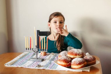 Sufganiyot yiyen çocuk, tatlı bayram yemekleri. Geleneksel Yahudi bayramı için menoralı bir kız. Hanuka Işık Festivali 'ni evde kutlayan bir çocuk. İsrail tatili.