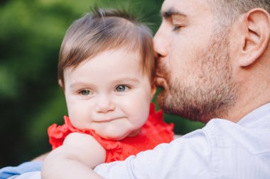 Babalar Günü. Orta yaşlı beyaz gururlu bir baba kucağında küçük kızını öpüyor. Açık havada parkta baba ve kızının yakın plan portresi. Çocuklu bir hayat. Mutlu bir aile hayatı..