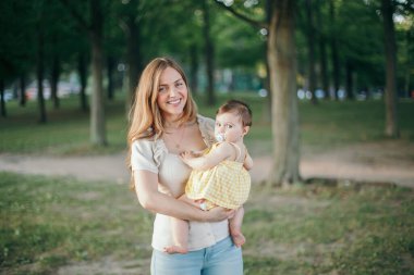 Anneler Günü. Orta yaşlı, gülümseyen beyaz anne ve kız çocuğu parkta oynuyorlar. Anne, yaz günü açık havada bebeğe sarılıyor. Otantik mutlu aile çocukluk hayatı.. 