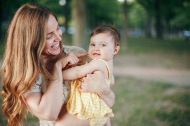Anneler Günü. Orta yaşlı, gülümseyen beyaz anne ve kız çocuğu parkta oynuyorlar. Anne, yaz günü açık havada bebeğe sarılıyor. Otantik mutlu aile çocukluk hayatı.. 