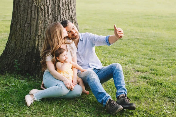 Making family memories. Happy parents mom and dad with baby girl daughter taking photo selfie with smartphone camera in park. Man, woman, baby talking on video chat call on cell phone outdoors.