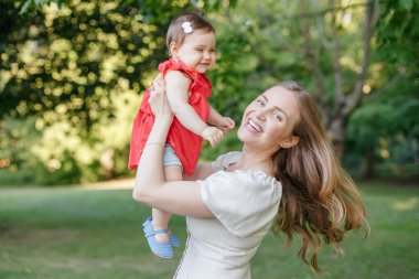 Anneler Günü tatili. Orta yaşlı, gülümseyen beyaz anne ve kız çocuğu parkta sarılıyorlar. Anne yaz günü açık havada bebek kucaklıyor. Mutlu otantik aile çocukluk hayatı. 