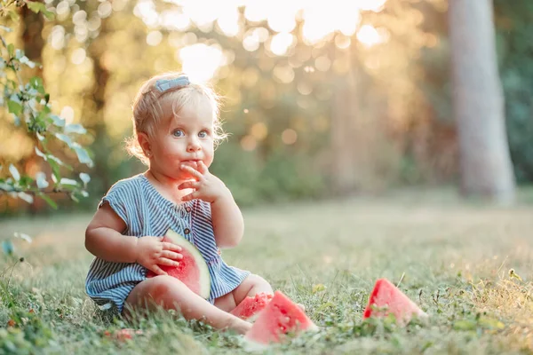 夏季野餐食品 可爱的白人女婴在公园里吃成熟的红色西瓜 有趣的小孩坐在地上 在户外吃新鲜的水果 幼儿补充健康手指食物 — 图库照片