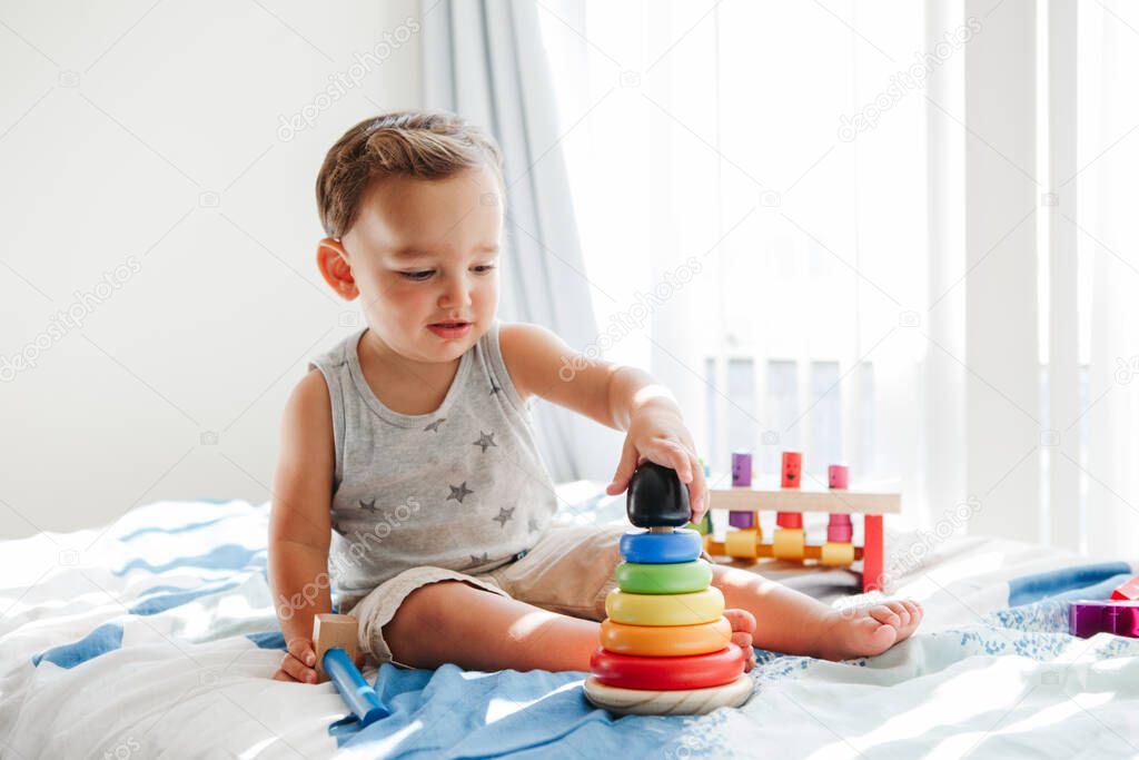 Cute baby toddler playing with learning toy pyramid stacking blocks at home. Early age Montessori education. Kids hand brain fun development activity for preschoolers.  