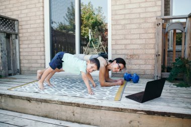 Aile sporu aktivitesi. Orta yaşlı beyaz bir anne ve yeni yürümeye başlayan oğlu uzaktan kumandalı uzaktan kumandalı bilgisayarla evin arka bahçesinde spor yapıyor. Ebeveyn, çocuk bebekle egzersiz yapıyor. Evde spor..