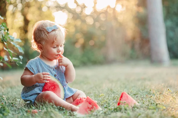 夏のピクニックフード 公園で熟した赤いスイカを食べるかわいい白人の赤ん坊の女の子 新鮮な果物を屋外で地面に座って面白い子供 幼児の子供のための固形健康的なフィンガーフード — ストック写真