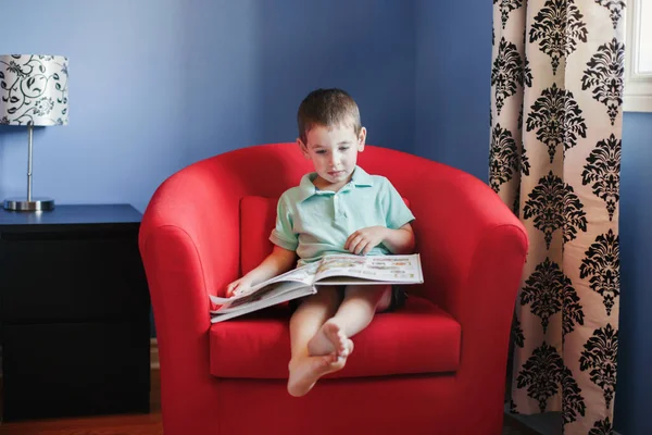 快乐的白人男孩坐在小孩房间的扶手椅上看书 幼儿发展和扫盲教育 真实的童年生活方式概念 — 图库照片