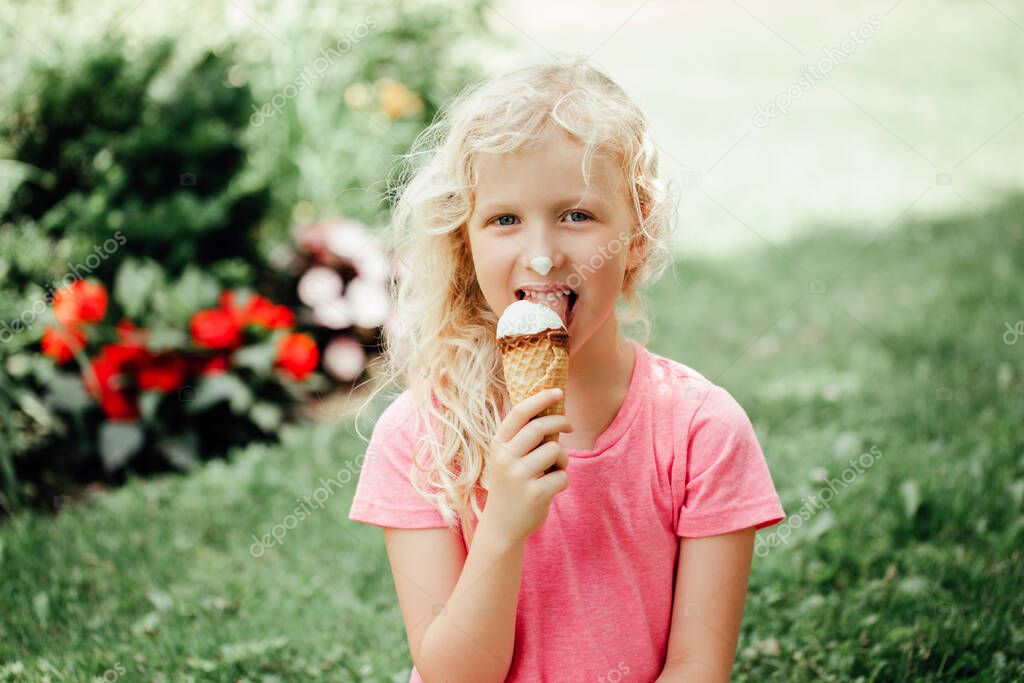 Cute funny adorable girl with long messy blonde hair eating licking ice cream from waffle cone. Child eating tasty sweet cold summer food outdoor. Summer frozen meal snack. 