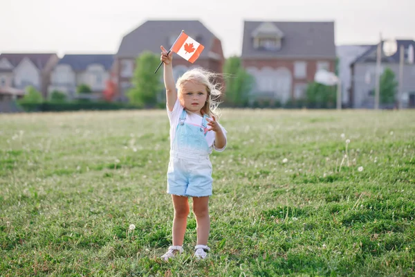 Happy Canada Day. Little blonde Caucasian toddler girl holding waving Canadian flag. Kid child citizen celebrating Canada Day outdoor on 1st of July.