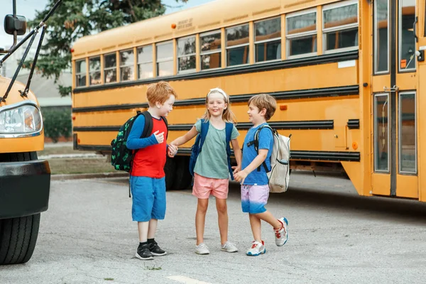 子供たち男の子と女の子の子供たち黄色のスクールバスの近くに立って話しています 夏休みの後に友達の同級生と会う 9月教育 学校へ戻る ストック写真