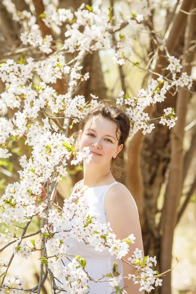 Närbild porträtt av vackra sexiga kaukasiska vuxen tjej kvinna med mörkt brunt hår och hassel ögon i vit klänning tittar i kameran bland blommande träd Sakura blommor i vår sommar — Stockfoto