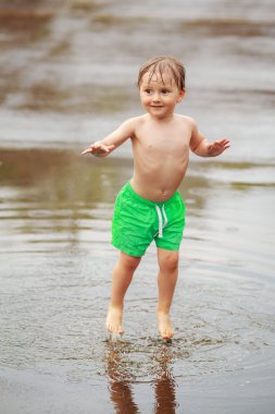 Çocuk su birikintileri yağmurun altında atlama