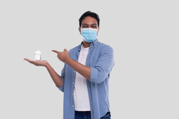 Man toont ontsmettingsmiddel op de hand en wijzen op het dragen van medische masker geïsoleerd. Indiase man draagt een medisch masker — Stockfoto