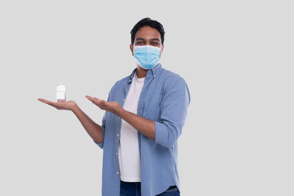 Homem mostrando anti-séptico na mão e apontando para ele vestindo máscara médica isolado. homem indiano vestindo máscara médica — Fotografia de Stock