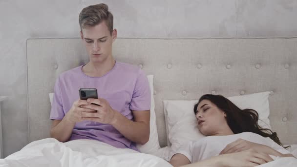 Man chat aan de telefoon terwijl het meisje slaapt. Man met telefoon in bed. Meisje slaapt in bed. Geschoten op rood. — Stockvideo