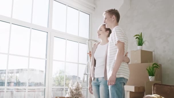 Casal Olhando pela janela lá dentro novo apartamento. Casal mudou-se para um novo lar. Um casal a viver num dia ensolarado. Tiro em vermelho — Vídeo de Stock