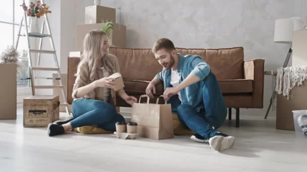 Pareja desempacando comida rápida en casa recién trasladada. Pareja teniendo comida de reparto. Nueva entrega a domicilio. Pareja comiendo comida rápida en casa. Disparo en ROJO — Vídeo de stock