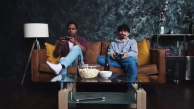 Arkadaşlar evde konsol oyunu oynuyorlar. Kanepede arkadaşlar. Evdeki oyuncular. Bira içmek.