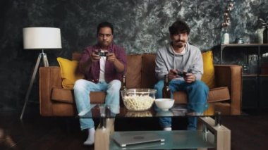 Arkadaşlar evde konsol oyunu oynuyorlar. Kanepede arkadaşlar. Evdeki oyuncular. Oyun oynayan adamlar. Hint adam oyunu kazandı.