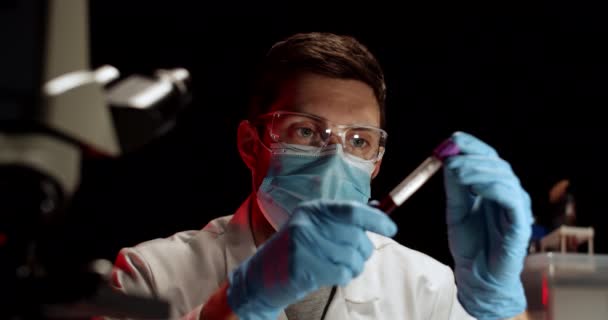 Arzt untersucht Bluttest in Flusk im Labor. Laborangestellte mit Blutprobe. Covid Test. Bluttest. Mann mit medizinischer Maske, Brille und Handschuhen. — Stockvideo
