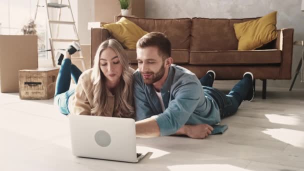 Couple Laying on the Floor in a New Home Using Laptop. Couple Using Laptop for Shopping, Booking Tickets, Discussing Interior. — Stock Video