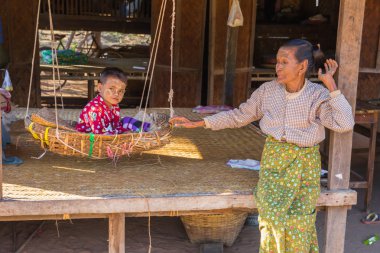 Child plays with his grandmother swinging in a hanging basket in its traditional home in a village of Bagan