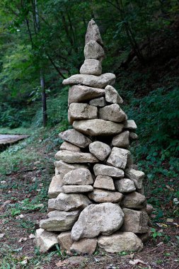 Yeşil ve taşlarla çevrili eski bir taş duvarın dikey görüntüsü.