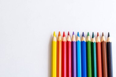 İzole edilmiş beyaz arka planda renkli kalemler. Metin veya imza için boş boşluk. Okulun beyaz masasına çeşitli renklerde malzemeler çizmek, yakın çekim. Alttan kalemler