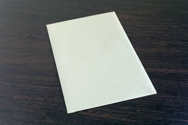 One blank sheet of paper on a brown wooden texture table with copy space. Design template blank sheet of paper on a dark background in office. New empty document. Watercolor paper mockup top view.