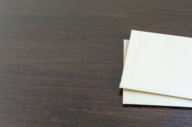 Koyu tahta bir masa yüzeyinde iki yeni boş kağıt. Ofis ya da eğitim konseptiyle tasarım için boş desen. Minimalizm örneği. Sol tarafta büyük bir kopya alanı var.