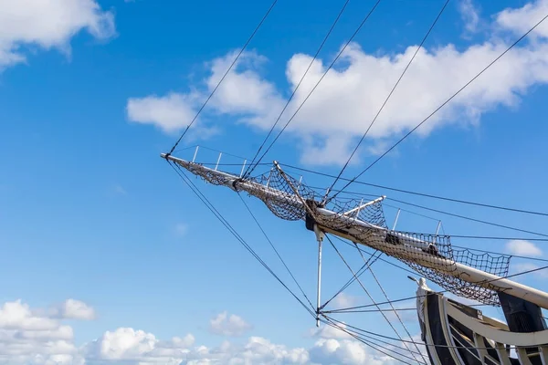 Forward head sailing mast of a wooden sailboat. Clear summer blue sky background with clouds with copy space. Old warship frigate mast. Maritime deck and ropes of a water transport. Regatta race theme