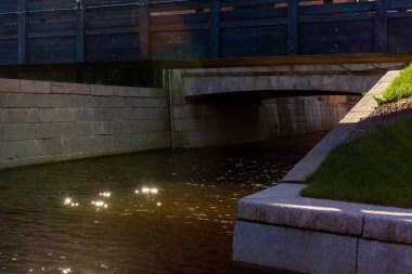 Şehir nehir kanalının su yüzeyinde inanılmaz bir güneş ışığı var. Taştan çevreler arasında güneşin kentsel dış yüzeydeki parlak yansımaları. Fotokopi alanı olan ahşap çit