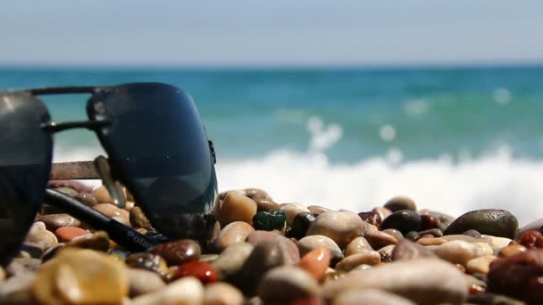 Gafas de sol en una playa de guijarros junto al mar . — Vídeos de Stock