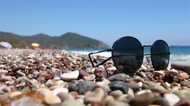 Сонцезахисні окуляри на гальковому пляжі біля моря . — стокове відео