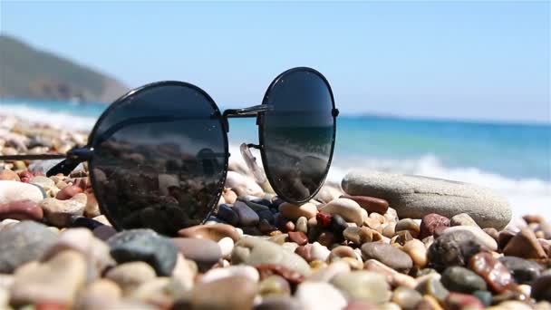Sunglasses on a pebble beach by the sea. — Stock Video