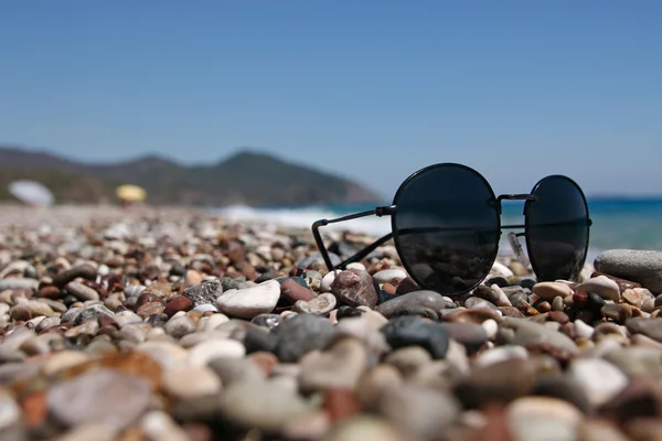 Deniz kenarında bir çakıl plajı üzerinde güneş gözlüğü. — Stok fotoğraf