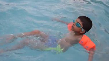 Havuzda yüzen mutlu Hintli çocuk, sıcak yaz tatillerinde hava tüpüyle birlikte yüzen çocuk, büyük bir havuzda yüzen çocuk..