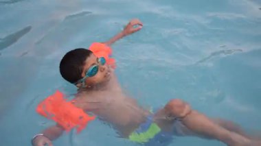 Havuzda yüzen mutlu Hintli çocuk, sıcak yaz tatillerinde hava tüpüyle birlikte yüzen çocuk, büyük bir havuzda yüzen çocuk..