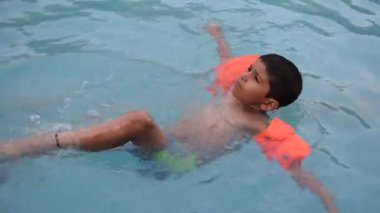 Havuzda yüzen mutlu Hintli çocuk, sıcak yaz tatillerinde hava tüpüyle birlikte yüzen çocuk, büyük bir havuzda yüzen çocuk..
