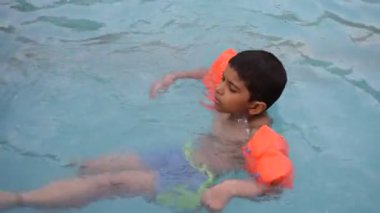 Havuzda yüzen mutlu Hintli çocuk, sıcak yaz tatillerinde hava tüpüyle birlikte yüzen çocuk, büyük bir havuzda yüzen çocuk..