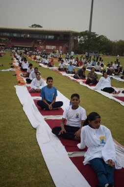 Yeni Delhi, Hindistan, 21 Haziran 2025 - Uluslararası Yoga Günü 'nde Delhi' deki Yamuna Spor Kompleksi 'nde grup Yoga egzersiz oturumu, kriket stadyumunda yoga sınıfına katılan büyük bir grup yetişkin